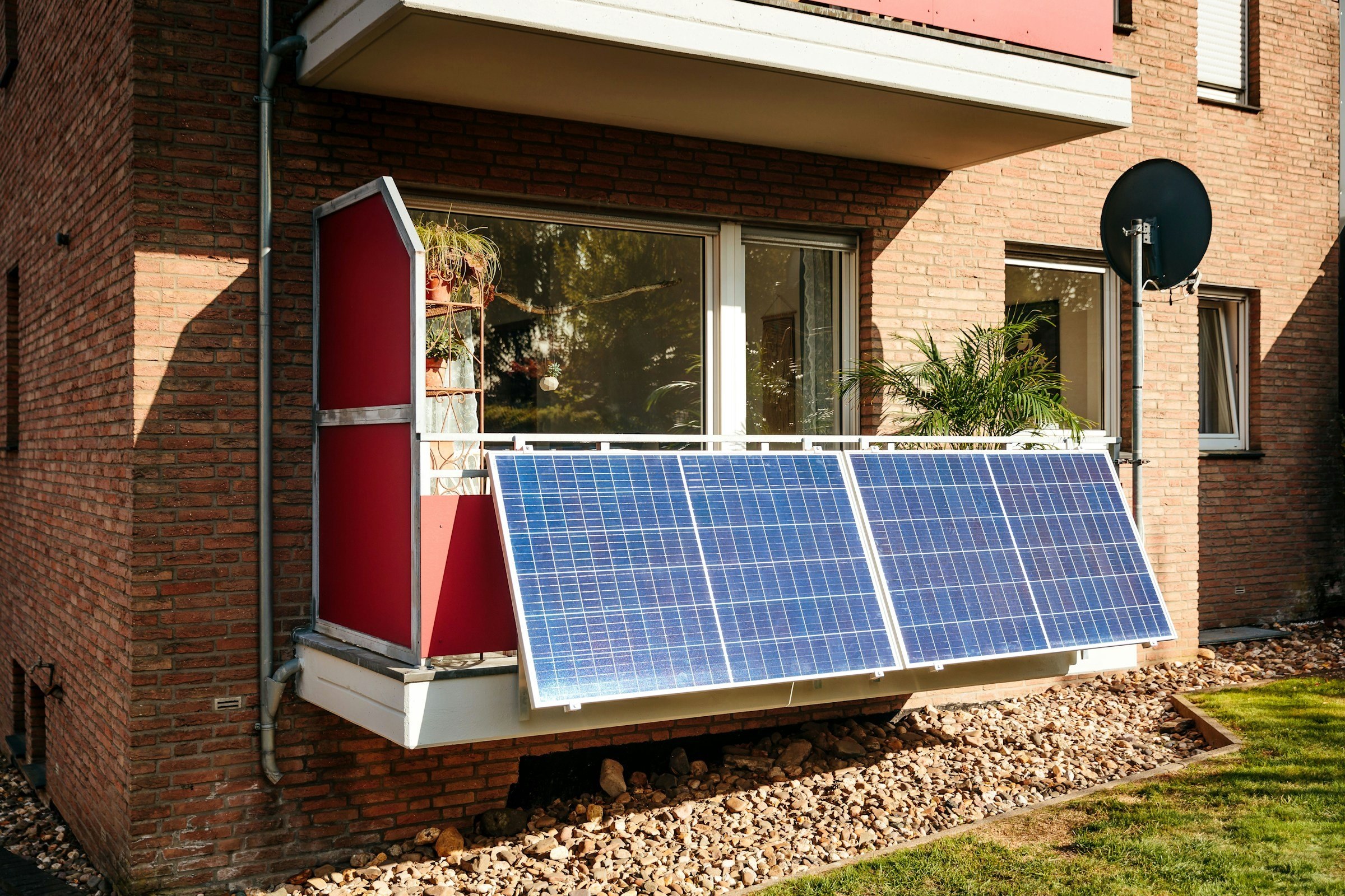 Zwei Solarmodule eines Balkonkraftwerks am Balkongeländer einer Erdgeschosswohnung in einem Mehrfamilienhaus aus Klinker