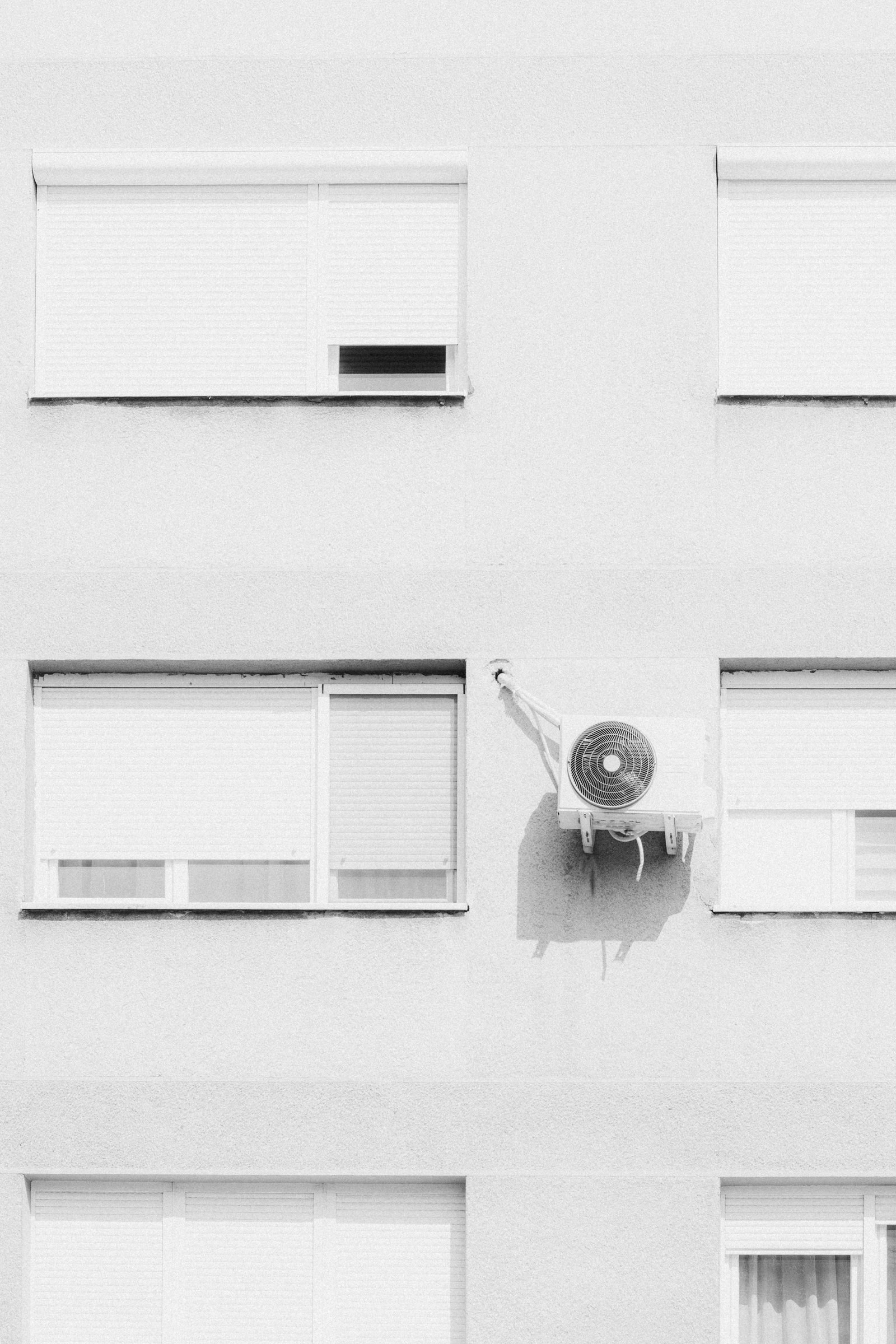 Helle Hausfassade mit Rollläden und einem an der Wand montierten Klimaanlagen-Außengerät, Schwarz-Weiß-Aufnahme